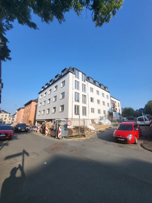 Massivholz-Mehrfamilienhaus als moderner Neubau an Straßenecke mit Baustellenabsperrung.