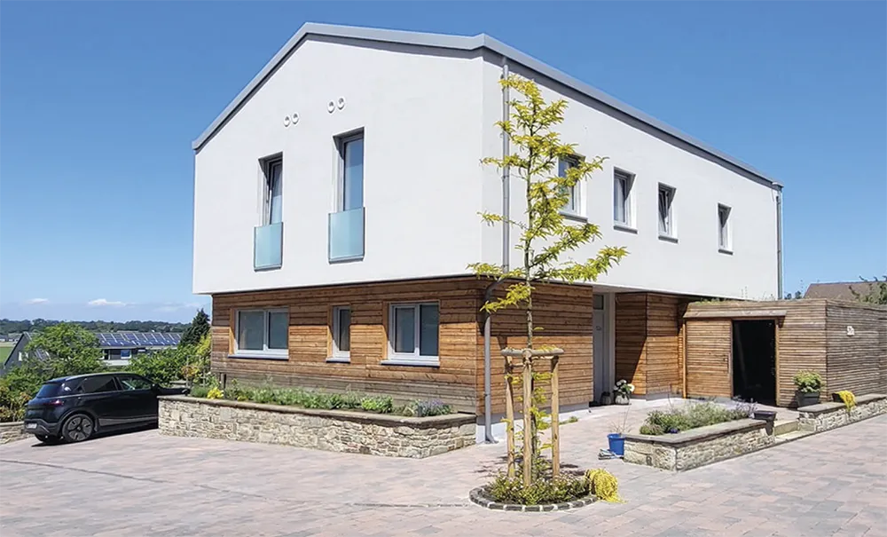 Modernes Massivholzhaus mit Holzfassade, weißem Obergeschoss und gepflasterter Einfahrt.