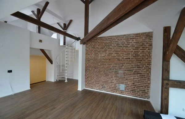 Renoviertes Loft im alten Schulgebäude mit Sichtziegelwand, Holzbalken und Wendeltreppe.