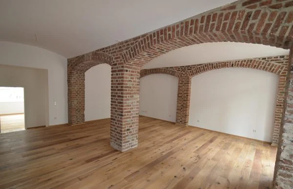 Sanierter Raum im alten Schulgebäude mit Backsteinbögen und Holzboden.