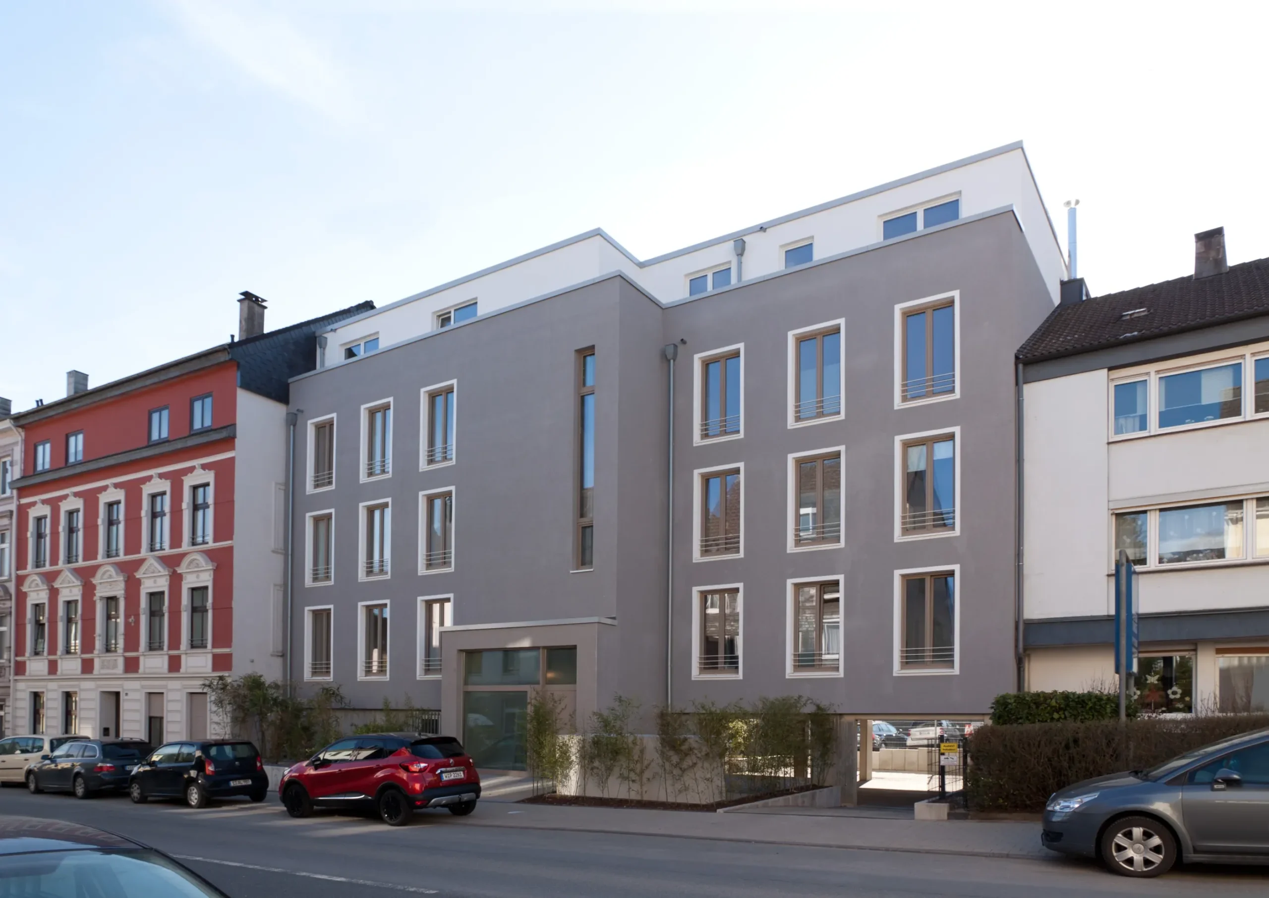 Modernes Wohngebäude mit Penthouse, Altbaufassaden und geparkten Autos in urbaner Straße.