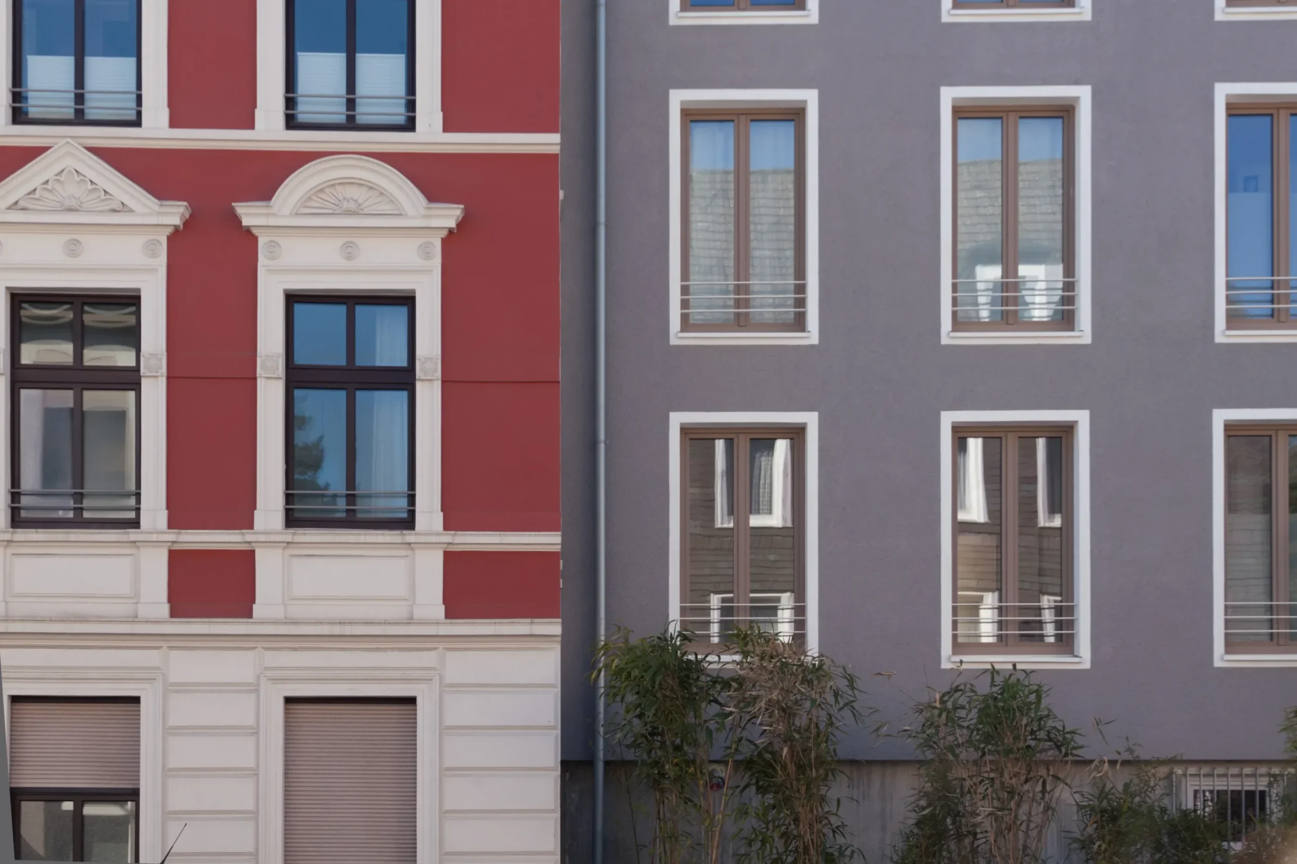 Historische rote und moderne graue Wohnhausfassade mit Fenstern und Zierdetails.