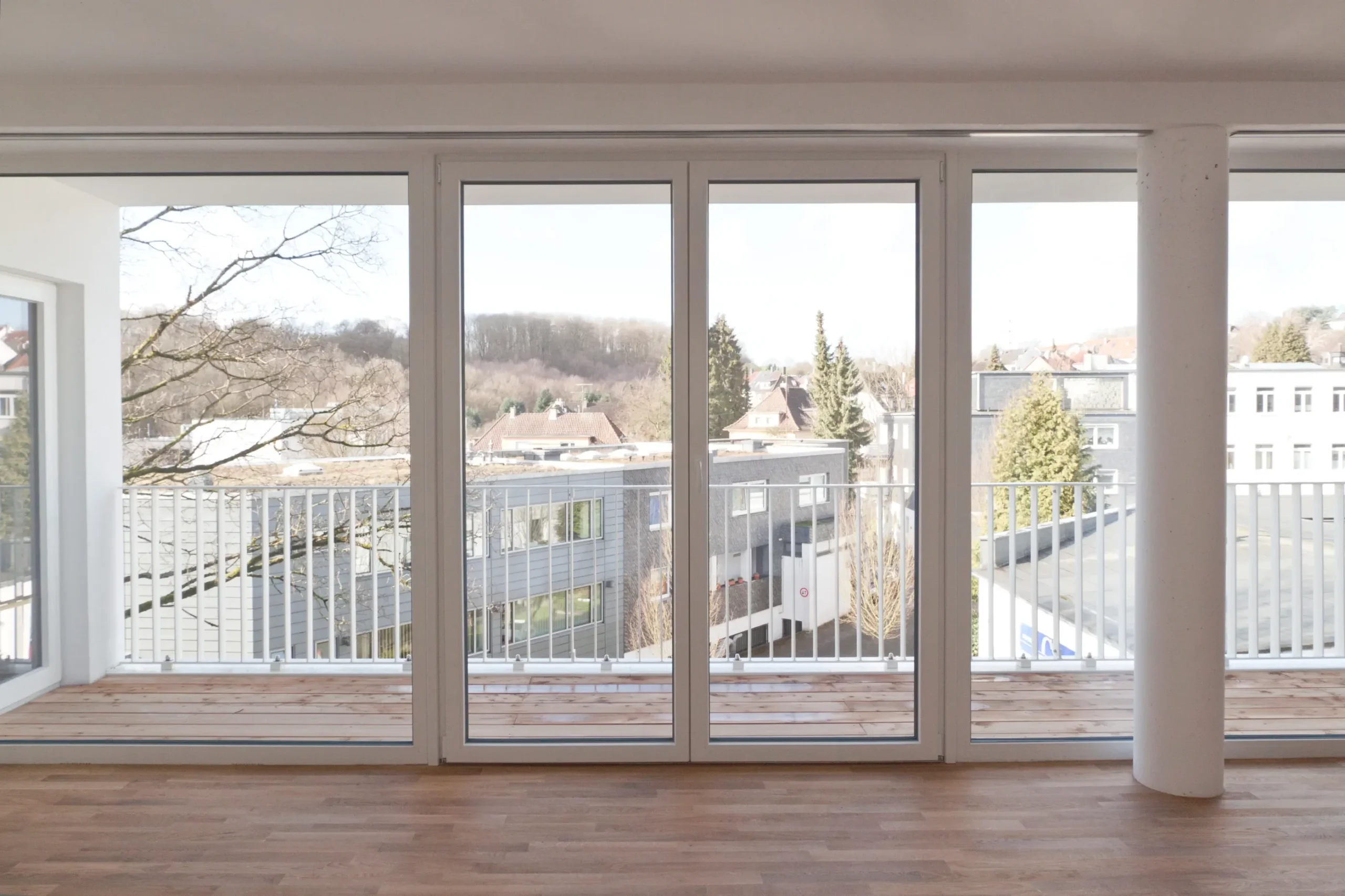 Moderner Wohnraum mit bodentiefen Fenstern, Balkon und Holzfußboden.