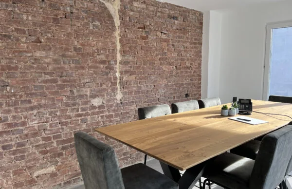 Moderner Besprechungsraum im Geschäftshaus Luisenstraße mit Holztisch, Backsteinwand und Tageslicht.
