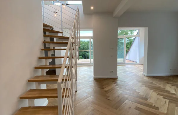 Modernes Wohninterieur mit geschwungener Holztreppe, Fischgrätparkett und Balkonblick.