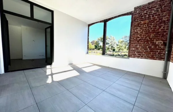 Heller Loft-Raum mit Ziegelwand, Fliesenboden und großer Fensterfront mit schöner Aussicht.