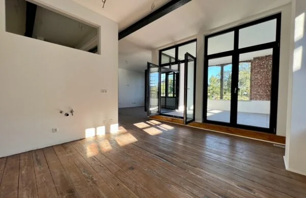 Helles Loft mit Holzboden, schwarzen Fensterfronten und Balkonzugang.