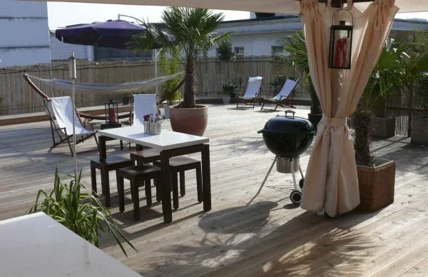 Dachterrasse eines Wohn- und Geschäftshauses in Wuppertal mit Grill, Lounge und Palmen.