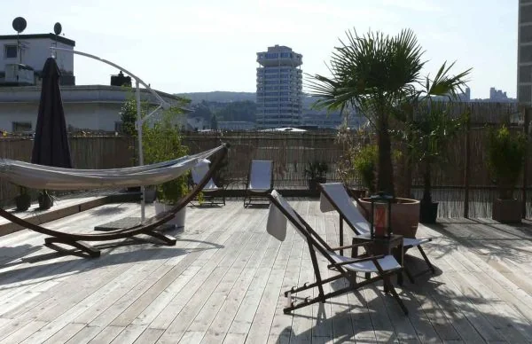 Sonnige Dachterrasse eines Wohn- und Geschäftshauses in Wuppertal mit Holzdeck, Liegestühlen und Stadtblick.